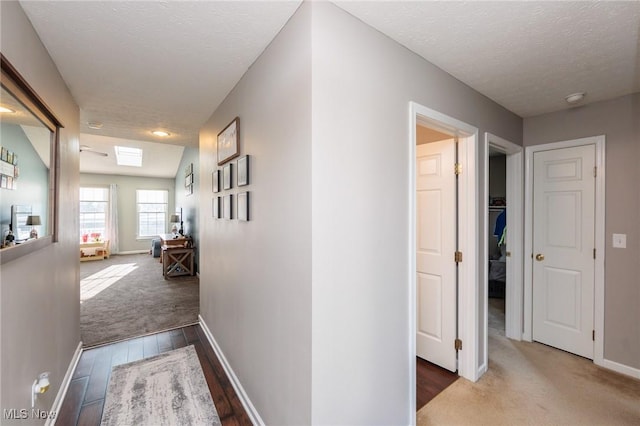 corridor with wood finished floors, baseboards, and a textured ceiling