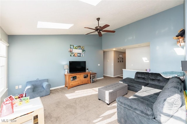 living area with baseboards, vaulted ceiling with skylight, a ceiling fan, and carpet flooring