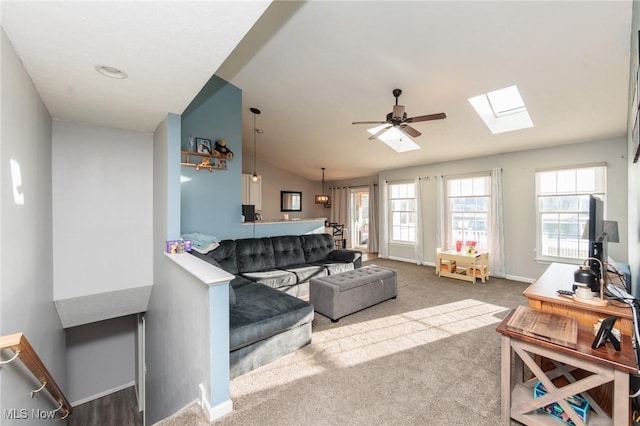 carpeted living room with baseboards, vaulted ceiling with skylight, and ceiling fan