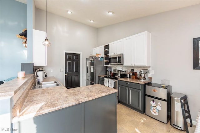 kitchen with light countertops, a peninsula, stainless steel appliances, white cabinetry, and a sink