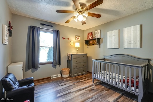 bedroom featuring wood finished floors, baseboards, visible vents, a nursery area, and a textured ceiling