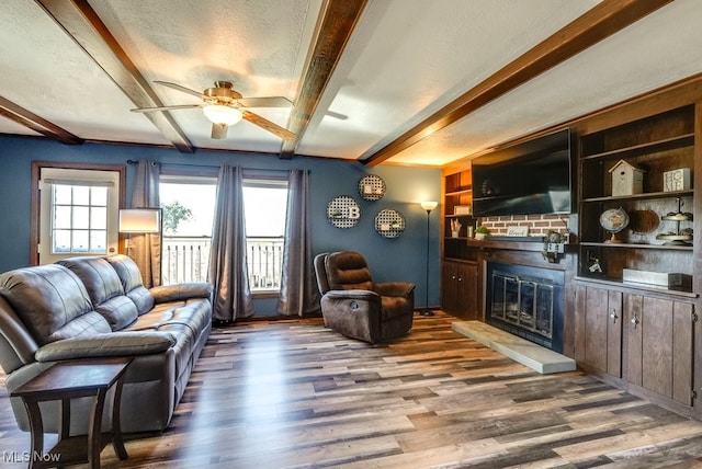 living room featuring beamed ceiling, a brick fireplace, wood finished floors, and a ceiling fan