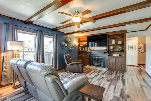 living room with beam ceiling, a glass covered fireplace, a ceiling fan, and wood finished floors