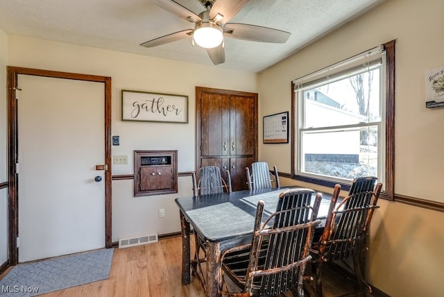 dining space with visible vents, a textured ceiling, light wood-style floors, baseboards, and ceiling fan