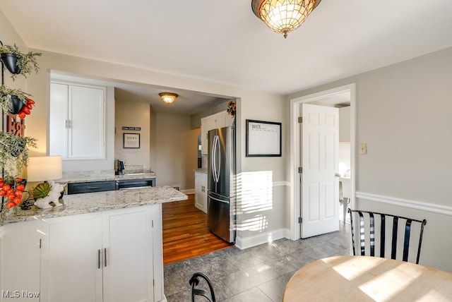 kitchen with light stone counters, freestanding refrigerator, a peninsula, white cabinets, and baseboards