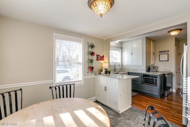 kitchen with light stone counters, a peninsula, stainless steel appliances, white cabinetry, and a sink