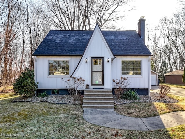 view of front of house with entry steps, roof with shingles, a chimney, a garage, and an outbuilding