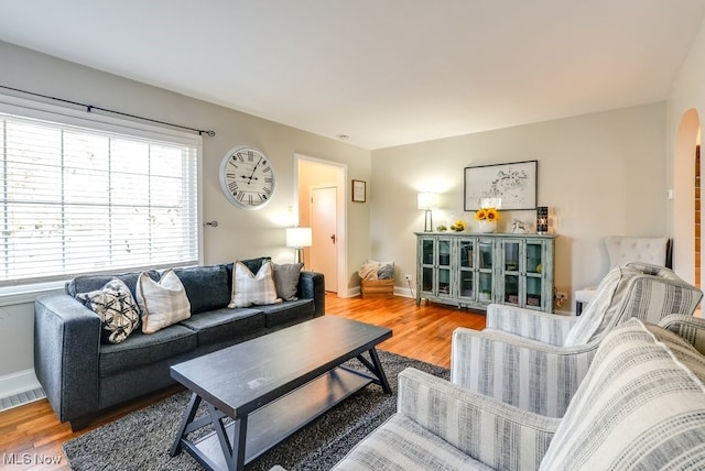 living room featuring wood finished floors, baseboards, and arched walkways