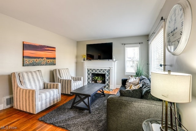 living area with a tiled fireplace, wood finished floors, visible vents, and baseboards