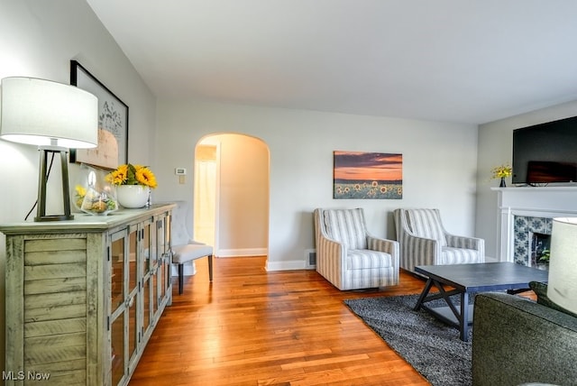 living area featuring visible vents, wood finished floors, arched walkways, a fireplace, and baseboards