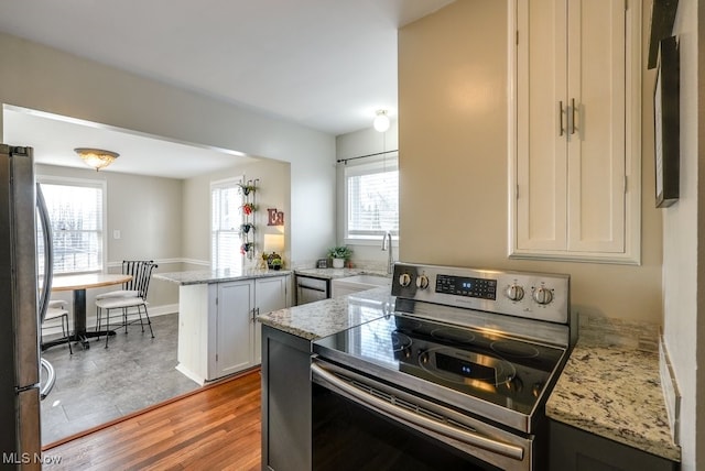 kitchen with a sink, light stone counters, stainless steel appliances, light wood-style floors, and a peninsula