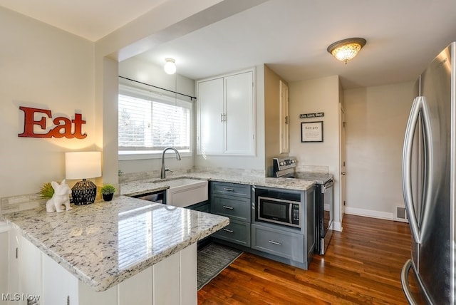 kitchen with visible vents, a sink, appliances with stainless steel finishes, a peninsula, and dark wood-style flooring