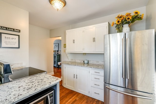 kitchen with wood finished floors, light stone countertops, arched walkways, stainless steel appliances, and white cabinetry