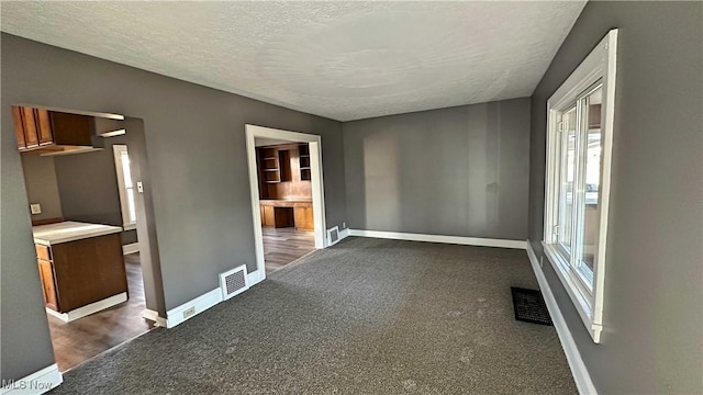 interior space with baseboards, visible vents, dark colored carpet, and a textured ceiling