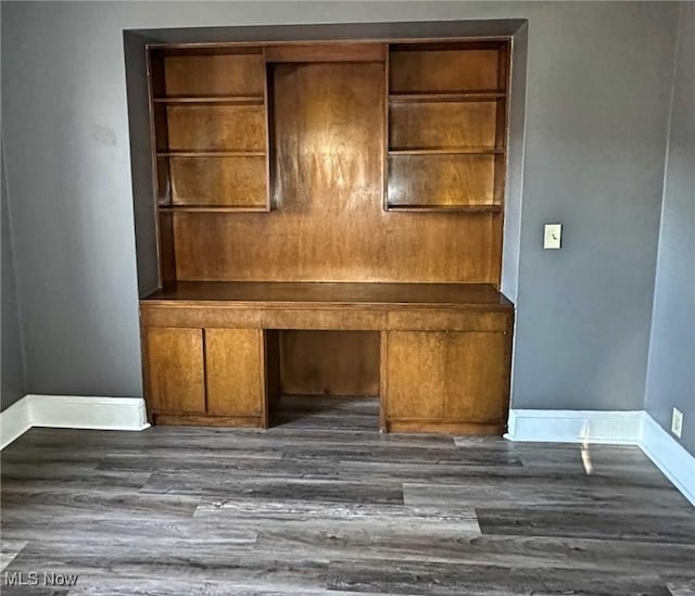 unfurnished office featuring dark wood finished floors, built in desk, and baseboards