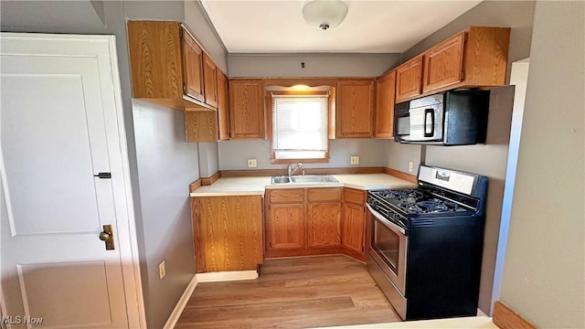 kitchen featuring gas range, brown cabinetry, black microwave, and a sink