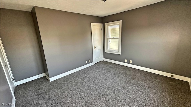 unfurnished room with a textured ceiling, baseboards, and dark colored carpet