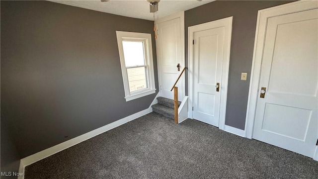 empty room with stairs, baseboards, a ceiling fan, and dark carpet