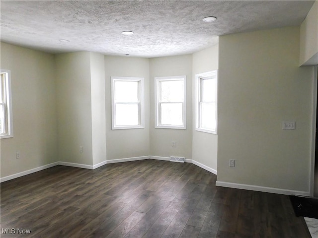 unfurnished room with visible vents, baseboards, a textured ceiling, and dark wood-style floors