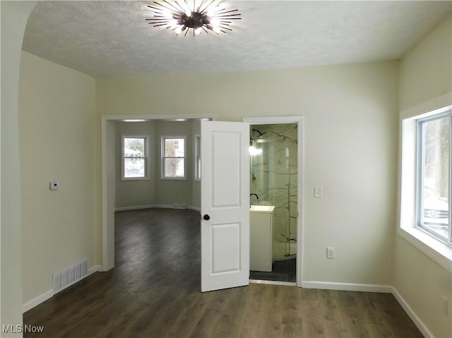 unfurnished bedroom featuring baseboards, visible vents, dark wood finished floors, ensuite bathroom, and a textured ceiling