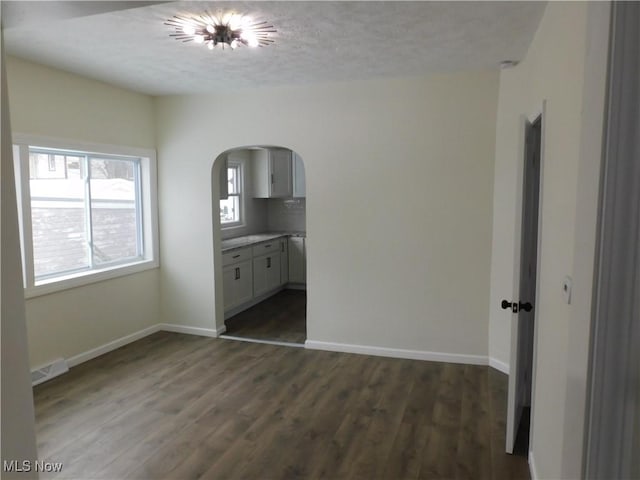 unfurnished bedroom featuring dark wood finished floors, baseboards, arched walkways, and a textured ceiling