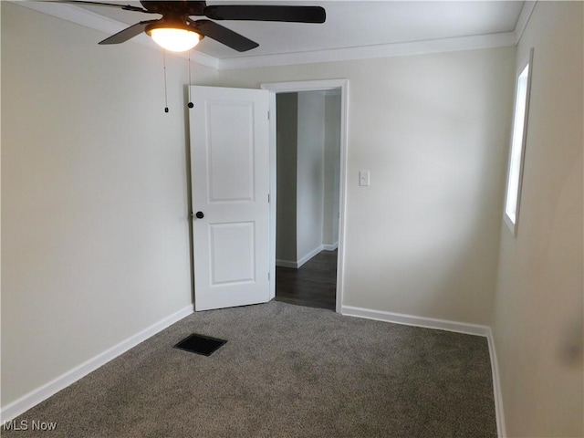 carpeted spare room featuring visible vents, ornamental molding, baseboards, a healthy amount of sunlight, and ceiling fan