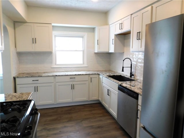 kitchen with dark wood-type flooring, a sink, light stone counters, appliances with stainless steel finishes, and decorative backsplash