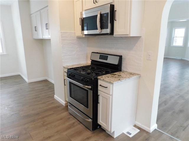 kitchen featuring light stone countertops, light wood-style flooring, arched walkways, appliances with stainless steel finishes, and tasteful backsplash