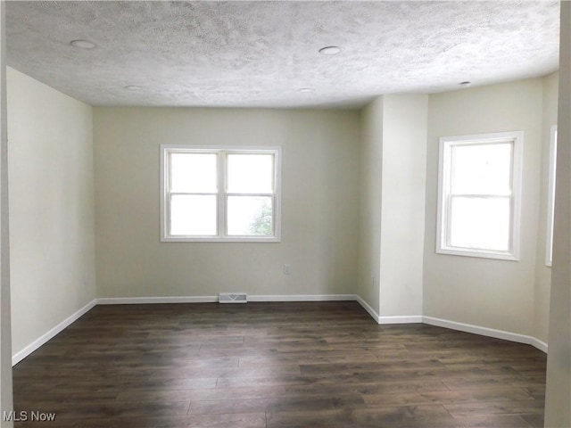 unfurnished room featuring visible vents, baseboards, dark wood-type flooring, and a textured ceiling