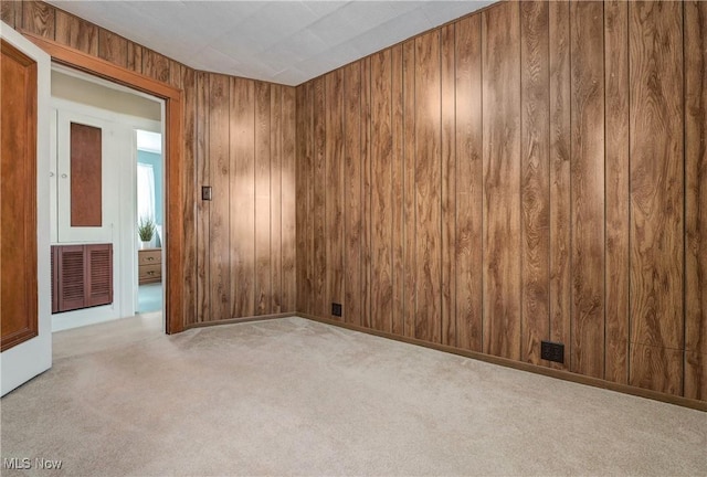 empty room featuring visible vents, baseboards, wood walls, and carpet flooring