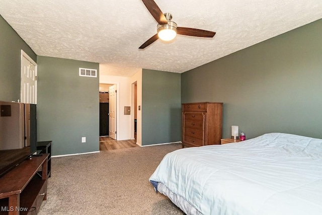 carpeted bedroom with ceiling fan, baseboards, visible vents, and a textured ceiling