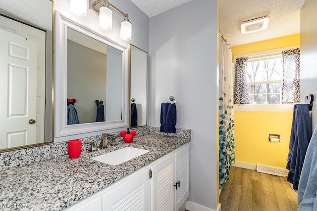 full bath featuring vanity, wood finished floors, visible vents, baseboards, and a textured ceiling