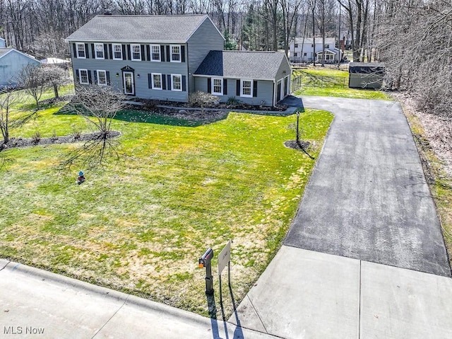 view of front of house featuring aphalt driveway, roof with shingles, a front yard, and fence