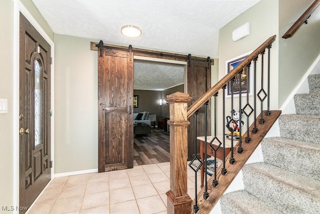 tiled entrance foyer featuring baseboards, a textured ceiling, stairs, and a barn door