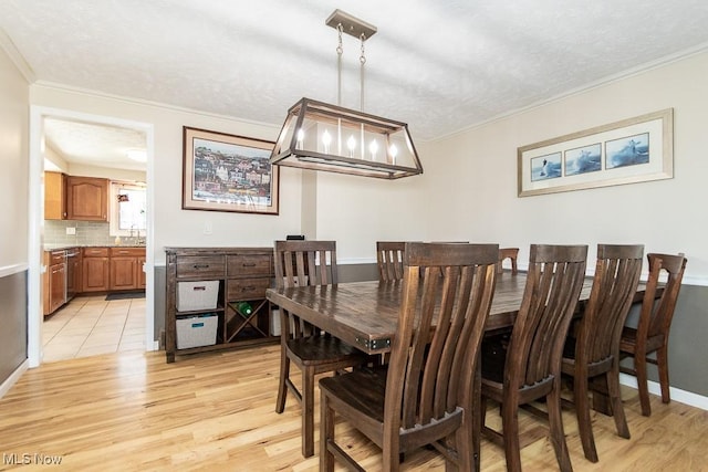 dining room featuring light wood-style flooring, a textured ceiling, baseboards, and ornamental molding