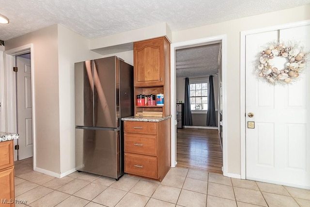 kitchen with light stone countertops, light tile patterned floors, freestanding refrigerator, brown cabinetry, and a textured ceiling