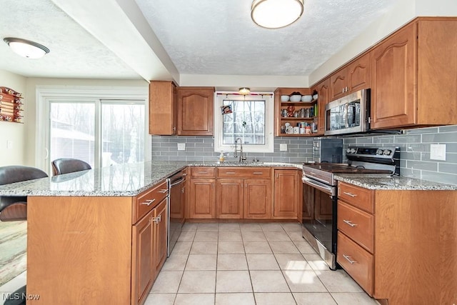 kitchen featuring brown cabinets, a kitchen breakfast bar, appliances with stainless steel finishes, a peninsula, and light stone countertops