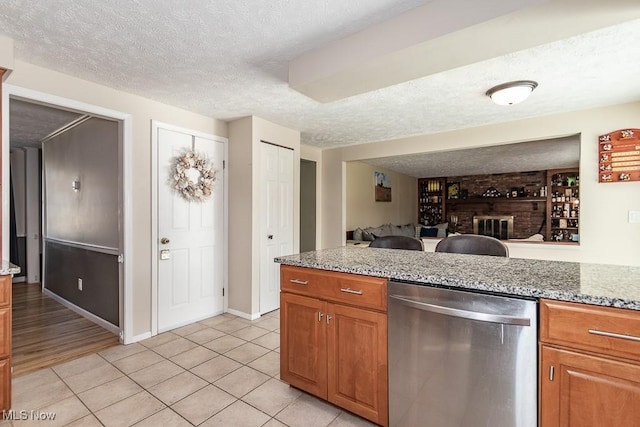 kitchen featuring dishwasher, light stone counters, a fireplace, and a textured ceiling