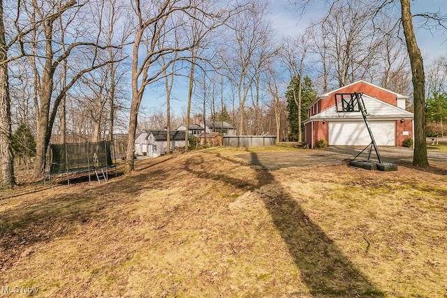 view of yard featuring a garage, driveway, an outdoor structure, and a trampoline