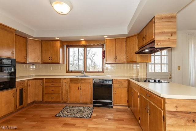 kitchen featuring brown cabinets, a peninsula, black appliances, and a sink