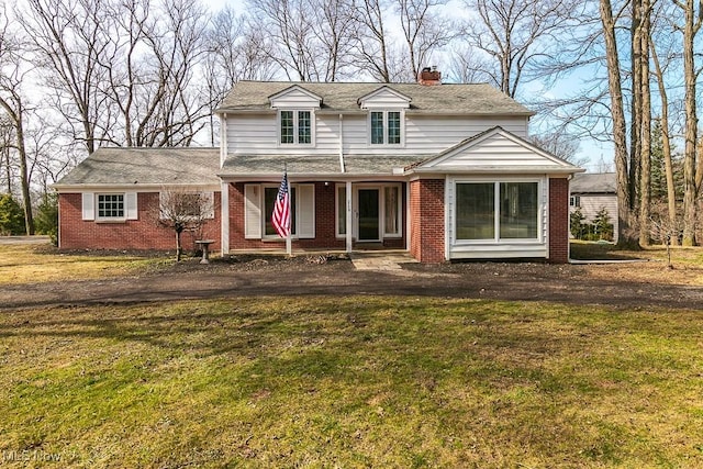 traditional home featuring a front yard, a porch, a shingled roof, a chimney, and brick siding