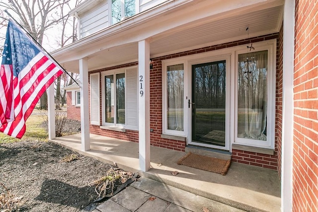 view of exterior entry with brick siding and a porch