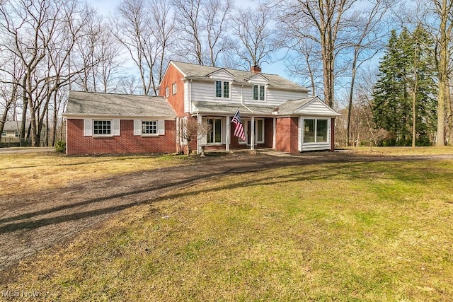 traditional home featuring a front yard, brick siding, driveway, and a chimney