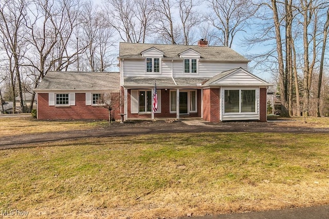 traditional home featuring brick siding, a front yard, and a chimney