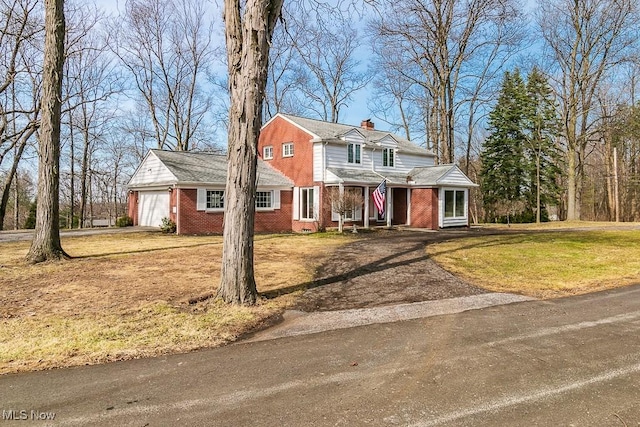 traditional-style house with brick siding, driveway, a chimney, and a front lawn