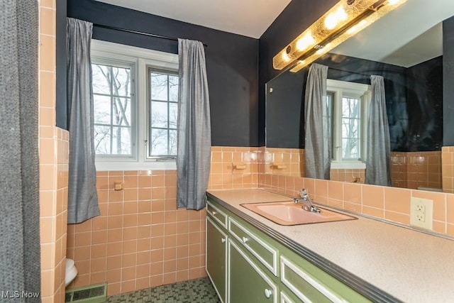 bathroom featuring vanity, tile walls, visible vents, and wainscoting