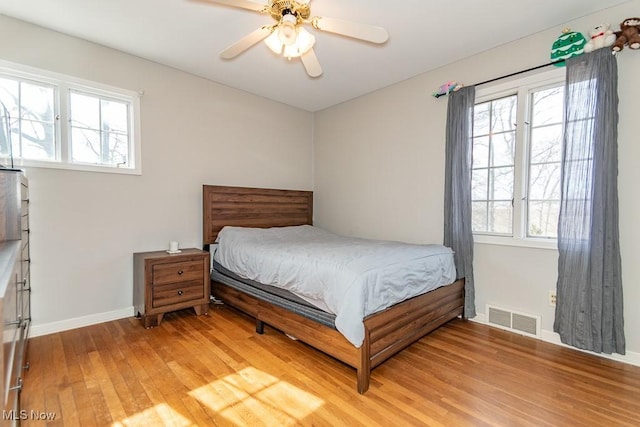 bedroom with ceiling fan, light wood-style floors, visible vents, and baseboards