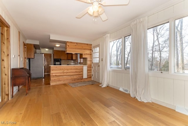 kitchen featuring visible vents, wall oven, light wood-style flooring, freestanding refrigerator, and brown cabinetry