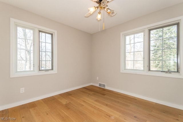 empty room with a wealth of natural light, visible vents, baseboards, and light wood finished floors