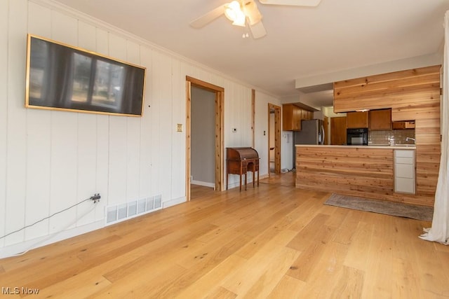 unfurnished living room with light wood-type flooring, visible vents, a ceiling fan, and crown molding